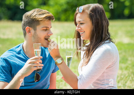 Frau Fütterung Traube zu ihrem Freund mit einem Glas Champagner in der Hand Stockfoto