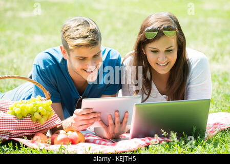 Glückliches Paar mit digitalen Tablet-PC und Laptop im Park Stockfoto
