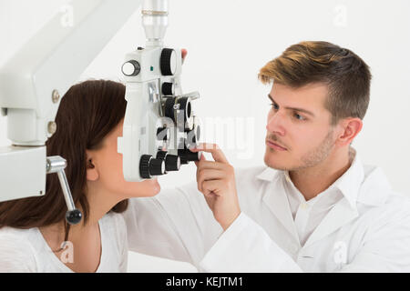 Ein männlicher Augenarzt einstellen Der phoroptor während der Prüfung die Augen der Patientin Stockfoto