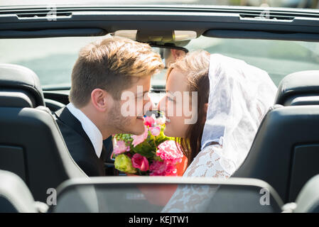 Frisch verheiratete junge lächelnde Paar küssen In die Hochzeit Auto Stockfoto