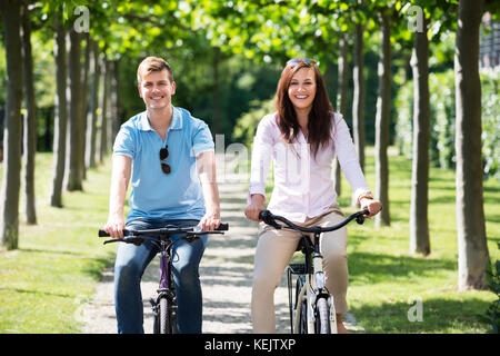 Portrait von Lächelnden jungen Paar genießt die Fahrt mit dem Fahrrad im Park Stockfoto