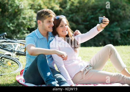 Glückliches Junges Paar unter Selfie auf Smart Phone im Park Stockfoto