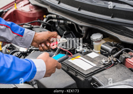 Nahaufnahme der Mechaniker Hände mit Multimeter zur Prüfung der Batterie im Auto. Stockfoto