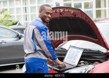 Junge glücklich Mechaniker mit Laptop mit einem offenen Auto Motor Stockfoto