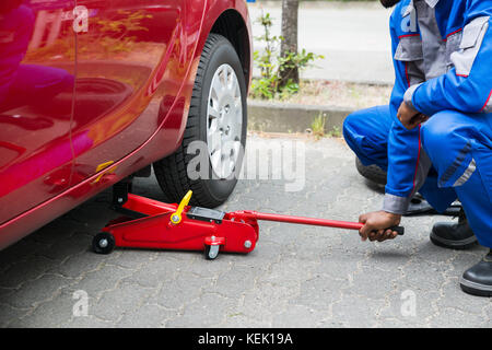 Junge männliche Mechaniker, Rot Hydraulische Wagenheber im Auto Stockfoto