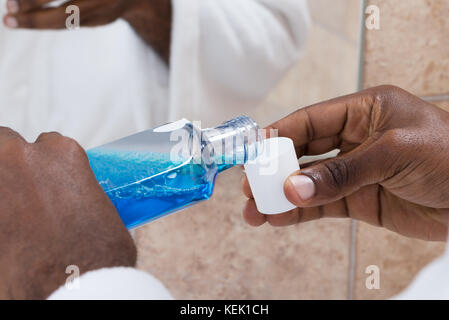 Nahaufnahme der Person Hände Gießen blaues Mundwasser in Ausgleichsbehälters Stockfoto