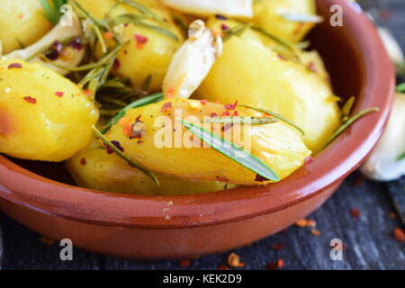 Ofen zubereitet Kartoffeln mit Rosmarin, Knoblauch, Olivenöl und Gewürzen in einem traditionellen Keramik Schüssel. mediterrane Lebensart. gesunde Ernährung Konzept. Stockfoto