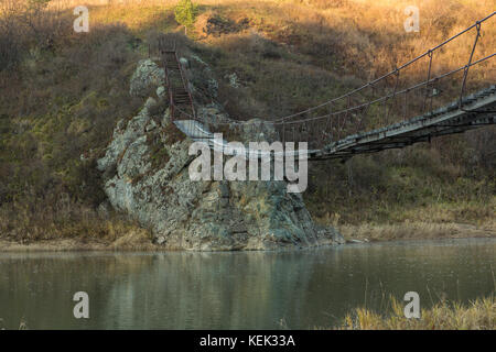 Die sehr alte hängende Fußgängerbrücke über einen kleinen Fluss. Stockfoto