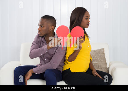 Traurig Paar zurück sitzen auf dem Sofa halten roten gebrochene Herzen zurück Stockfoto