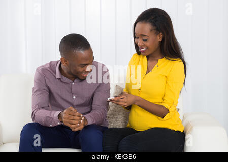 Junge schwangere Paare sitzen auf einem Sofa an der Schwangerschaft Test suchen Stockfoto