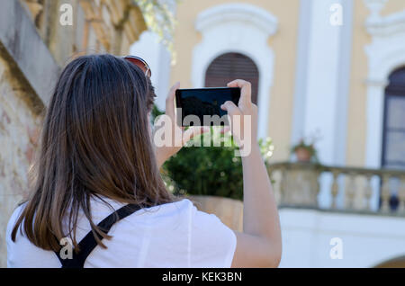 Eine Rückansicht einer jungen Frau mit Sonnenbrille fotografieren ein altes Gebäude in die Natur mit einem unscharfen Hintergrund Stockfoto