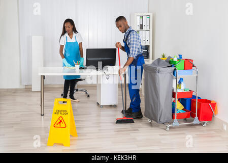 Junge männliche und weibliche Reiniger Reinigung Büro mit nassen Boden Warnschild auf dem Boden Stockfoto