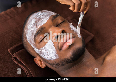 Therapeuten, die Gesichtsmaske zu den jungen afrikanischen Mann in Spa Stockfoto