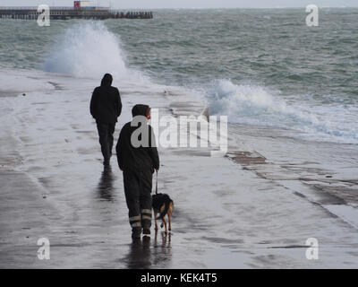 Southsea, Portsmouth, Großbritannien. Oktober 2017. Wetter in Großbritannien. Ein Mann geht mit seinem Hund entlang der Southsea Promenade, während Wellen über die Meeresmauer von Southsea brechen, während Sturm Brian bei Flut die Südküste Großbritanniens trifft. Quelle: simon evans/Alamy Live News Stockfoto