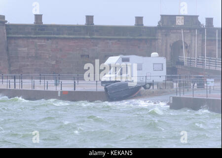 New Brighton, Wirral, Großbritannien. 22 Okt, 2017. Urlauber in Reisemobile sind unbeirrt, wie starker Wind und Regen eine einsame New Brighton, auf dem Wirral Peninsula, folgenden Sturm Brian getroffen. Ein kleines Boot hat sich gegen das Geländer durch das Wetter geworfen worden. Credit: Paul Warburton/Alamy leben Nachrichten Stockfoto