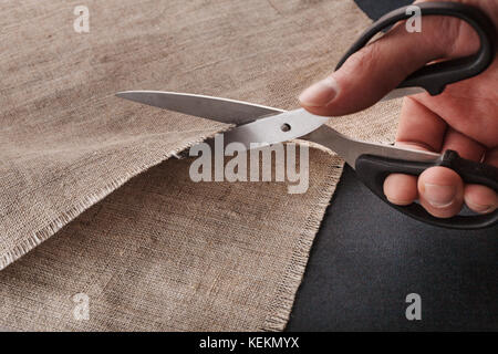 Hand schneidet ein Leinentuch mit der Schere zuschneiden. Stockfoto