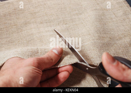 Hand schneidet ein Leinentuch mit der Schere zuschneiden. Stockfoto