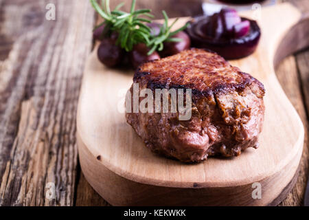 Leckeres Rindfleisch Filet Mignon serviert auf Holz Schneidebrett mit gerösteten Zwiebeln und Rosmarin Stockfoto