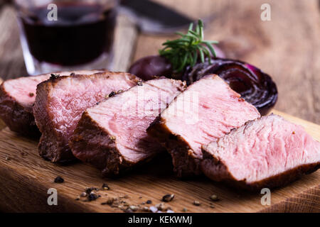 Leckeres Rindfleisch Filet Mignon serviert auf Holz Schneidebrett mit gerösteten Zwiebeln und Rosmarin Stockfoto