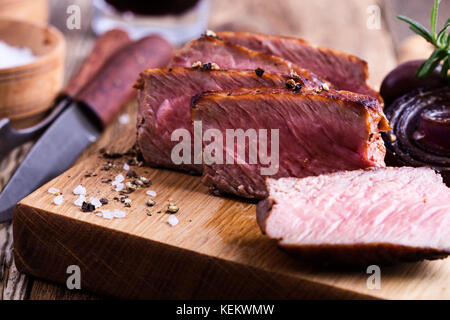 Leckeres Rindfleisch Filet Mignon serviert auf Holz Schneidebrett mit gerösteten Zwiebeln und Rosmarin Stockfoto