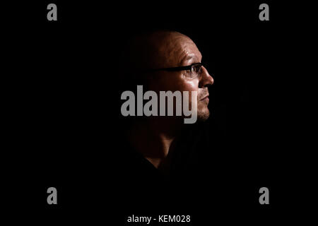 Seite Profil von einem weißen Mann mittleren Alters mit Brille oder Glas, die in Schatten vor einem schwarzen Hintergrund, blickte in Richtung des Lichts GROSSBRITANNIEN Stockfoto