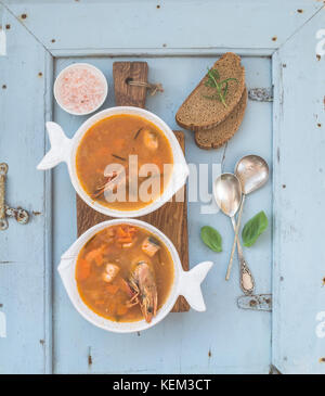 Französische Bouillabaisse fisch Tomatensuppe mit Lachsfilet, Garnelen und Gewürzen auf rustikalen Holzbrett auf hellblauem Hintergrund, Ansicht von oben Stockfoto