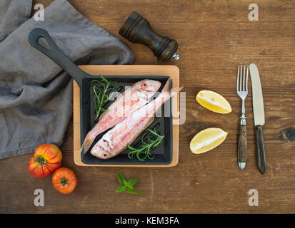 Roh ungekocht Rotbarbe Fisch in einem kochenden Topf mit Rosmarin, Zitrone und Knoblauch über rustikal Hintergrund, Ansicht von oben Stockfoto