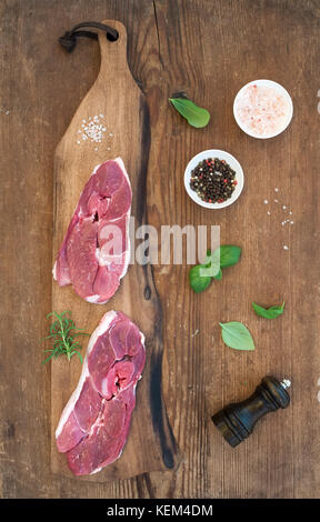 Rohe frische Fleisch Lamm Entrecote und Würzmittel auf Schneidebrett mit rustikalen Holzmöbeln Hintergrund. Stockfoto