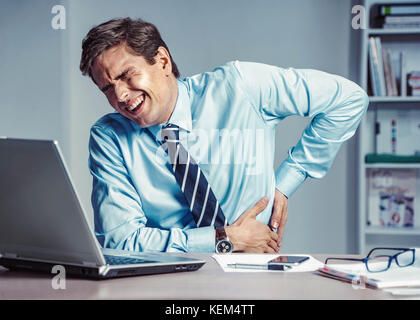 Mitarbeiter leidet unter starken Schmerzen im Rücken. Foto der Mann bei der Arbeit im Büro. medizinisches Konzept. Stockfoto