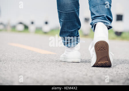 Nahaufnahme, Frau tragen Jean und weiße Sneaker vorwärts zu Fuß auf der Autobahn unterwegs in sonniger Tag, allein reisen oder Alleinreisende Konzept. Stockfoto