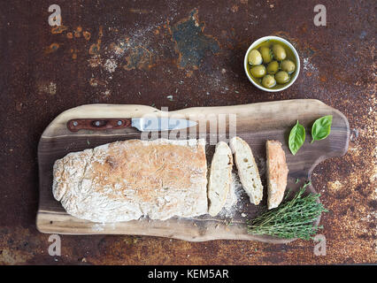 Frisch gebackene hausgemachten Ciabatta Brot mit Oliven, Basilikum und Thymian auf Nussbaum Holz Brett über grunge Rostiges Metall Hintergrund, Ansicht von oben Stockfoto