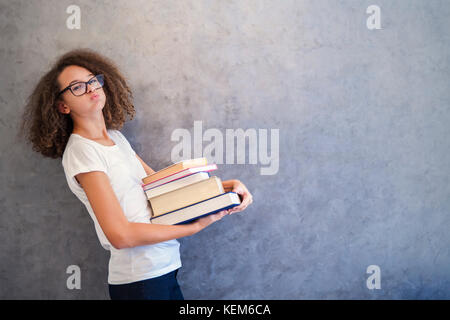 Portrait von jugendlichen Mädchen mit Brille steht neben der Wand und hält mehrere Bücher Stockfoto