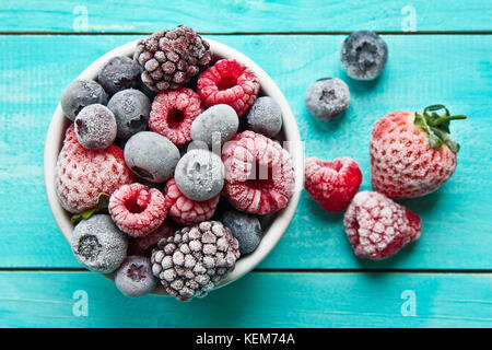 Verschiedene gemischte gefrorene Beeren in einer Schüssel auf blauem Hintergrund Stockfoto