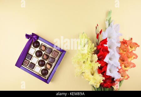 Wunderschöne gladiolen Blumen auf Gelb mit köstlichen Pralinen in Geschenkbox. Stockfoto