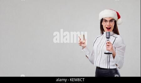 Eine Frau in einem Santa Claus hat singt ein Karaoke in das Mikrofon. Stockfoto