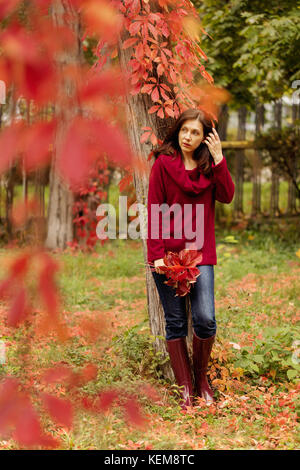 Junge Frau (BRÜNETT) in Jeans, Pullover und crimson Gummistiefel ist zu Fuß in einem Herbst Park. Selektive konzentrieren. Stockfoto