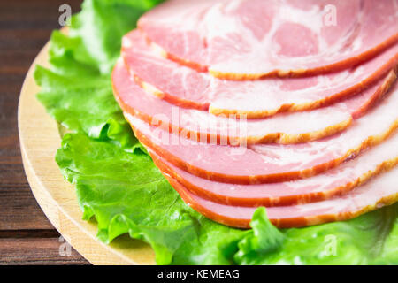 Schinken mit frischen grünen Salatblätter auf einem runden Schneidebrett. Fleischerzeugnisse auf braunem Holz- Tabelle. Stockfoto