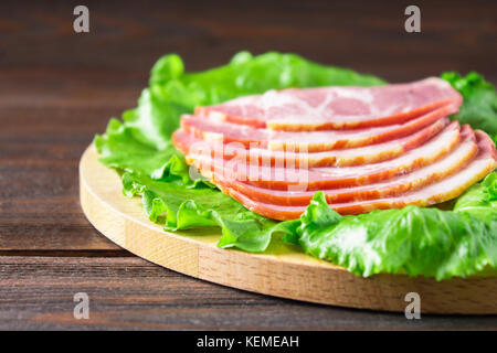 Schinken mit frischen grünen Salatblätter auf einem runden Schneidebrett. Fleischerzeugnisse auf braunem Holz- Tabelle. Stockfoto