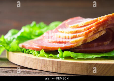 Schinken mit frischen grünen Salatblätter auf einem runden Schneidebrett. Fleischerzeugnisse auf braunem Holz- Tabelle. Stockfoto