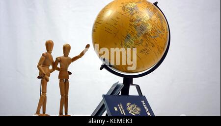 Zwei hölzerne Figuren stehen neben einem Globus und zwei Pässe. Eine Abbildung ist auf der ganzen Welt Stockfoto