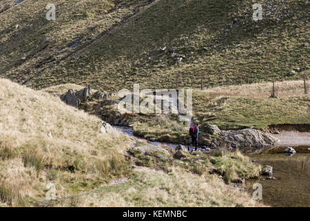 Ein Walker überquert den Bach am kleinen Wasser über haweswater im Eden Valley im Lake District Stockfoto