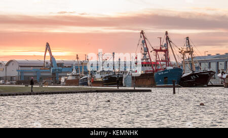 22. Oktober 2017; Shoreham Port, Sussex, UK; zwei Männer Fisch im Hafen vor eine Flotte von fischtrawler. Es ist ein buntes Dämmerung Himmel Stockfoto