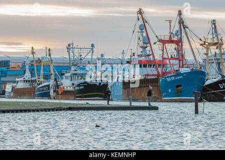 22. Oktober 2017; Shoreham Port, West Sussex, UK; zwei Männer mit Stangen im Anschluss kurz nach Sonnenaufgang. Flotte der Trawler, die im Hintergrund liegt. Stockfoto