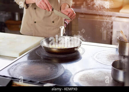 Koch schneiden Zwiebel in die Pfanne. männliche Küchenchefs an professionelle Küche schneiden Zwiebel in einer Pfanne mit gedünstetem Gemüse. kulinarische Küche und Konzept Stockfoto