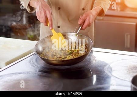 Hände von Chef Rühren dünsten Gemüse. Chef an der professionellen Küche im Restaurant kochen Gemüse. Der Prozess der vegetabes schmort. Stockfoto