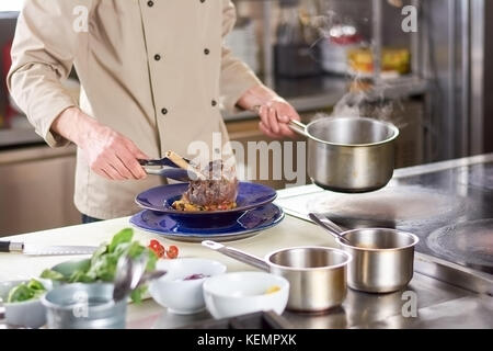 Koch, Lammkeule in der Platte. zugeschnittene Bild der männlichen Koch puttete Schaft von Lämmern in Platte. Küchenchef kochen Fleisch mit Gemüse an prfessional Küche. Stockfoto