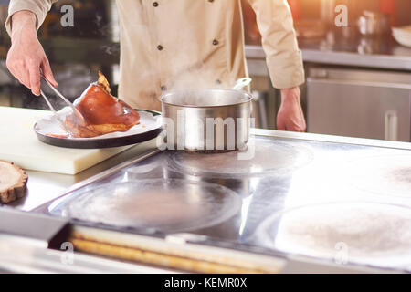 Frisch gekochte Schaft von Lamm. männliche Koch setzen auf großes Stück gekochte Lammkeule auf Weiß. Stockfoto