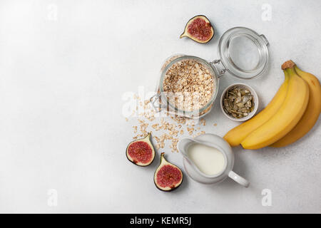 Zutaten für das Frühstück: Haferflocken, Milch, Feigen, Bananen, Kürbiskerne. Ansicht von oben Stockfoto