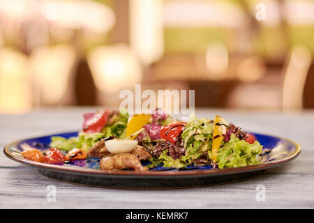 Wachtel mit grünem Salat auf blauen Platte. appetitlich Warmer Salat mit wachtel Schlachtkörper und Fleisch auf verschwommenen Hintergrund. Stockfoto