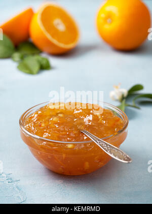 Orange Marmelade in eine Glasschüssel, frische Orangen auf blauem Hintergrund. Stockfoto